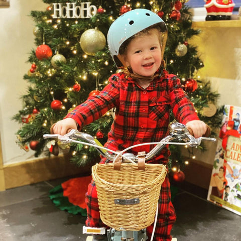 little boy in pyjamas on a bobbin bike with a bobbin helmet in front of a christmas tree