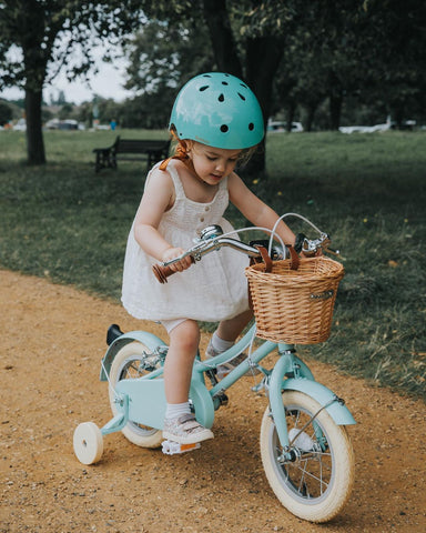 little girl in dress on blue bobbin bike with a matching helmet in a park
