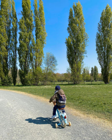 little boy on stabiliser bike with tall trees on open path