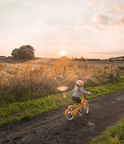 girl cycling on yellow bike on country path by wheat fields